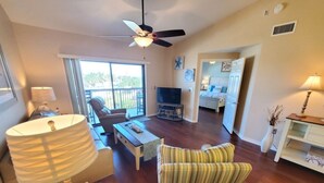 A spacious living area with a ceiling fan, a television, a sofa, and a dining table. - Ocean Villae Club I35: Soothing Ocean Village 2BR: Elevator & Pools (St. Augustine)