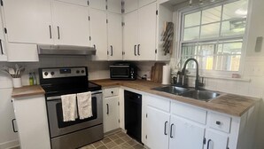 Una cocina compacta con gabinetes blancos, horno de acero inoxidable, microondas y lavavajillas.