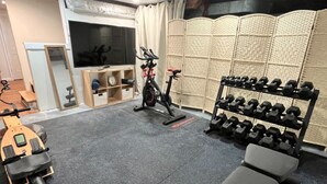 Un gimnasio con equipo de ejercicio, incluyendo una bicicleta estática, mancuernas y una máquina de remo.
