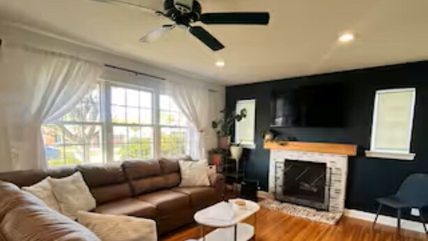 Una sala de estar con un sofá marrón, una mesa de centro blanca, una chimenea y un ventilador de techo.