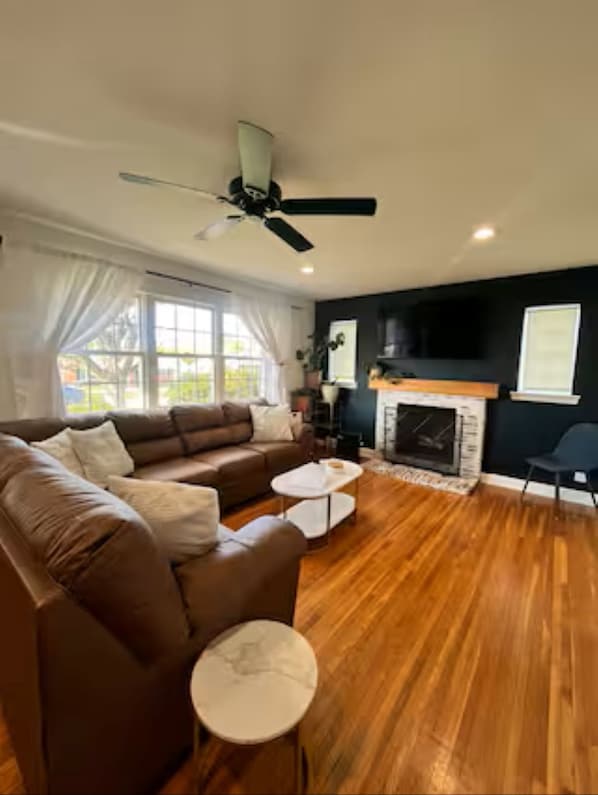 A living room with a brown sofa, a white coffee table, a fireplace, and a ceiling fan.
