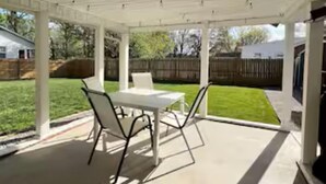 Un patio techado con mesa y sillas, un techo con luces y vista a un jardín trasero.