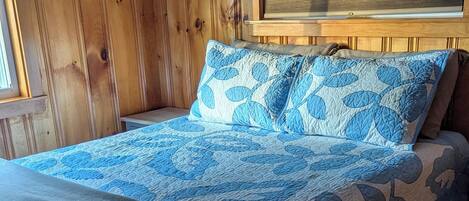 A wooden-paneled room with a bed featuring a blue and gray patterned bedspread and pillows.