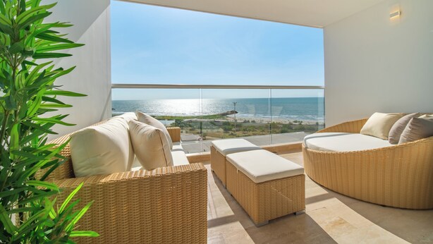 Un balcón con mobiliario de mimbre, vistas al mar y una planta.