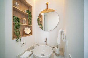 A bathroom with a round mirror, wooden shelves with plants, a white sink, and a towel rack. - Sophisticated Beach front with  lovely Cartagena de Indias (Cartagena de Indias)