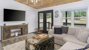 A living room with a large flat-screen TV, a wooden cabinet, a beige sofa, and a rustic trunk. - Welcome Hunters! Next to Garrity Mtn Wildlife Area (Anaconda)