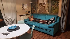Una sala de estar con un sofá azul, una mesa redonda blanca y una pequeña mesa de comedor.