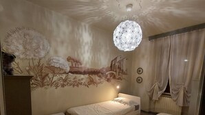 Un dormitorio con una cama individual, una mesita de noche pequeña, un velador y un techo decorativo con una lámpara colgante.