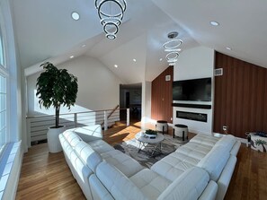 A modern living room with a large sectional sofa, a potted plant, and a flat-screen TV mounted on the wall. - Catskills Escape! Hot Tub, Massage Chairs & Games (Round Top)