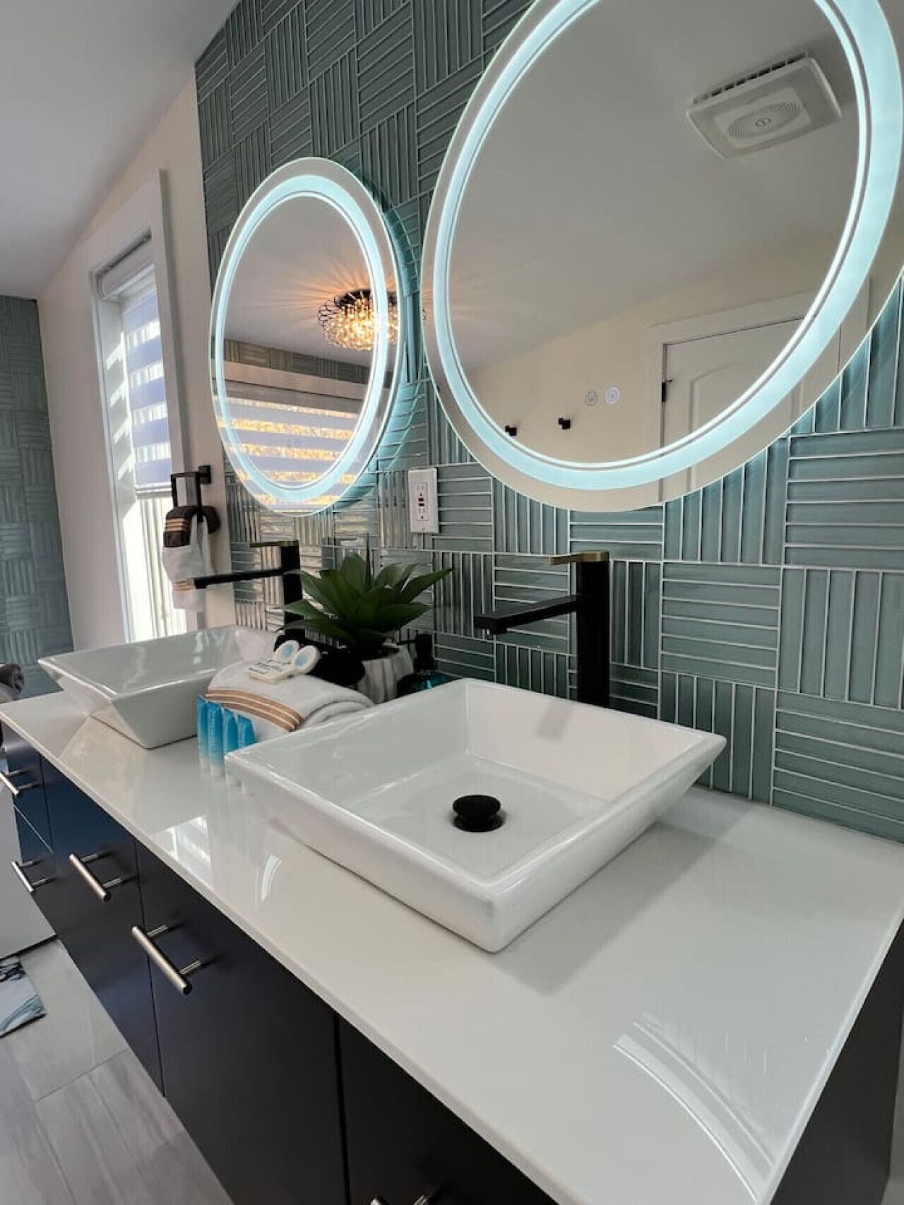 A modern bathroom with two sinks, a large mirror, and a decorative light fixture.