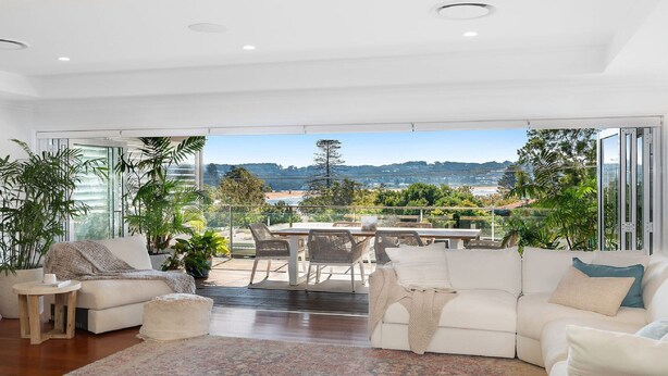 A spacious living room with a large glass door leading to a balcony with a view of the beach and hills. - Whitewater - Stylish Beach House With Ocean Views (AVOCA BEACH)