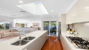 A modern kitchen with a central island, stainless steel sinks, and a gas stove. - Whitewater - Stylish Beach House With Ocean Views (AVOCA BEACH)