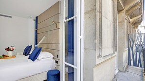 Una habitación de hotel moderna con una cama, un taburete pequeño y una ventana con vistas a la calle.