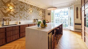 A modern kitchen with a large island, wooden cabinets, and a patterned wall. - Luxery 4Bedroom Apart_Near Arch of Triomphe_With AC & Outbuilding for staff (Paris)