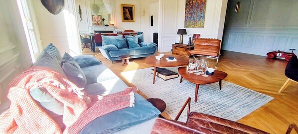A spacious living room with a sofa, a coffee table, and a dining area with a table set for a meal. - Luxery 4Bedroom Apart_Near Arch of Triomphe_With AC & Outbuilding for staff (Paris)