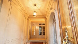 A grand hallway with a chandelier, a wooden door with a brass handle, and a red doormat. - Luxery 4Bedroom Apart_Near Arch of Triomphe_With AC & Outbuilding for staff (Paris)