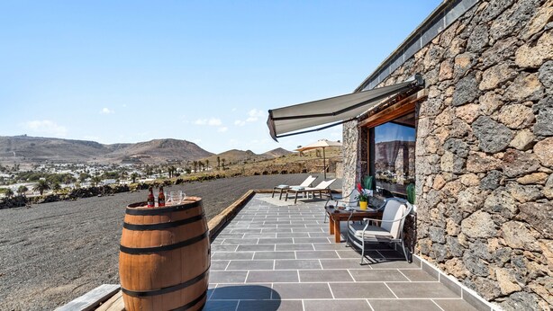 Un patio con baldosas de piedra, un barril de madera y mobiliario exterior.