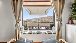 Un balcón con vista a una colina, una mesa con sillas y una planta en maceta.