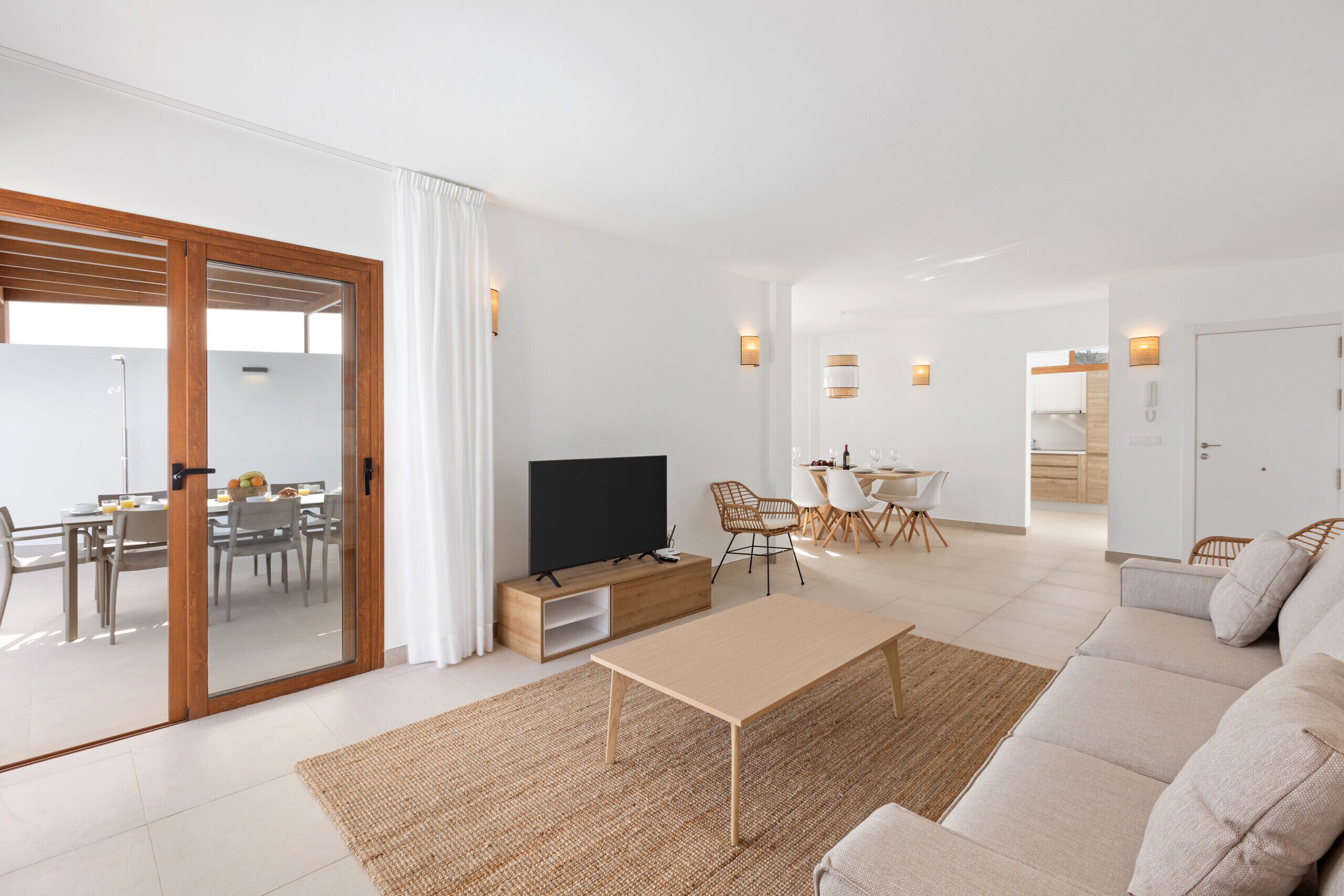 Una sala de estar moderna con sofá, mesa de centro, televisor y comedor con sillas y mesa.