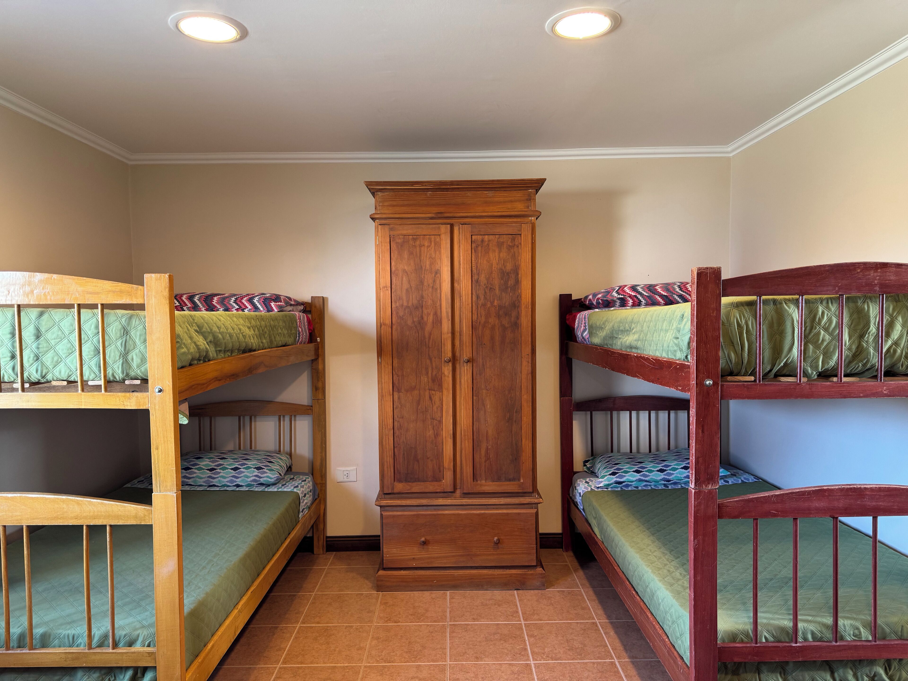 A dormitory room with two bunk beds, a wooden wardrobe, and a tiled floor.