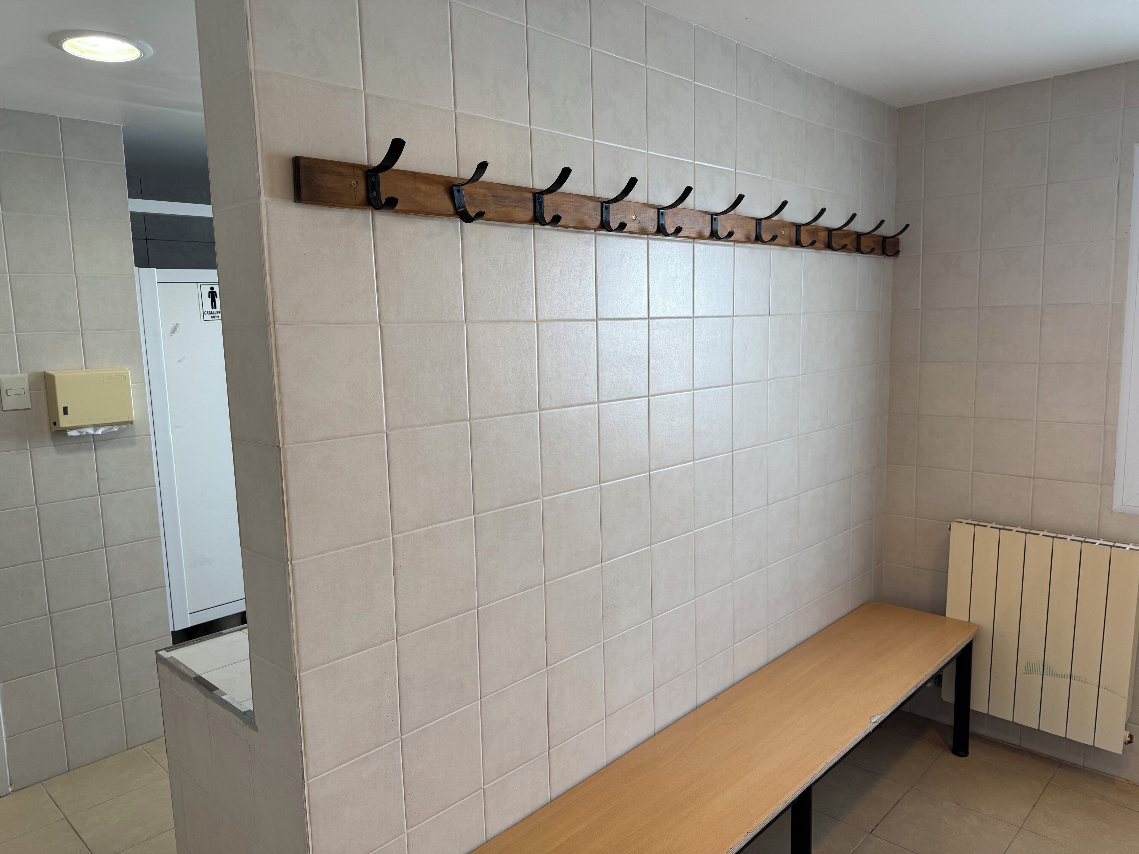 A bathroom with a bench, a towel rack, and a hand dryer.