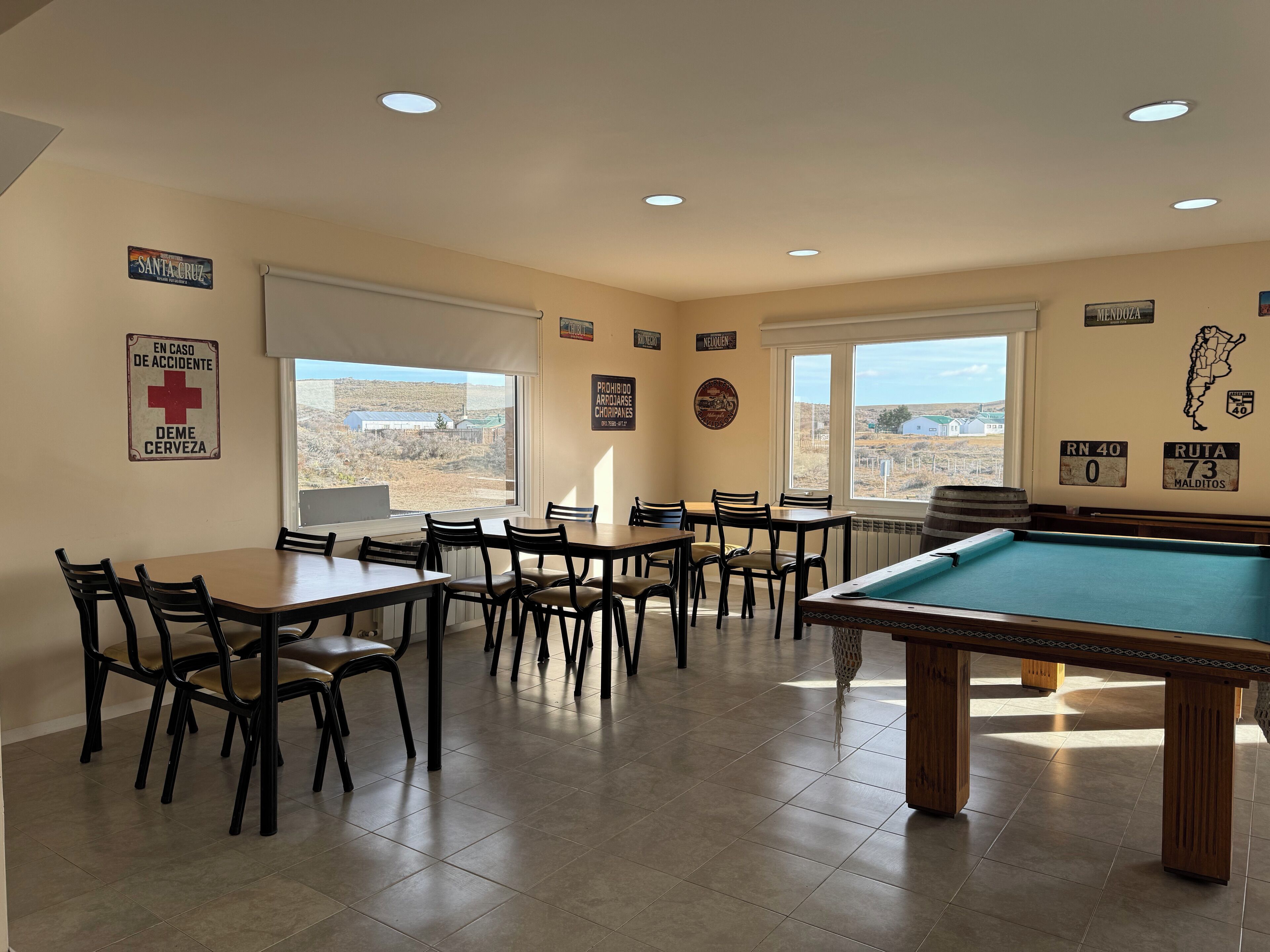 A room with a pool table, multiple tables, chairs, and large windows offering a view of the desert landscape.