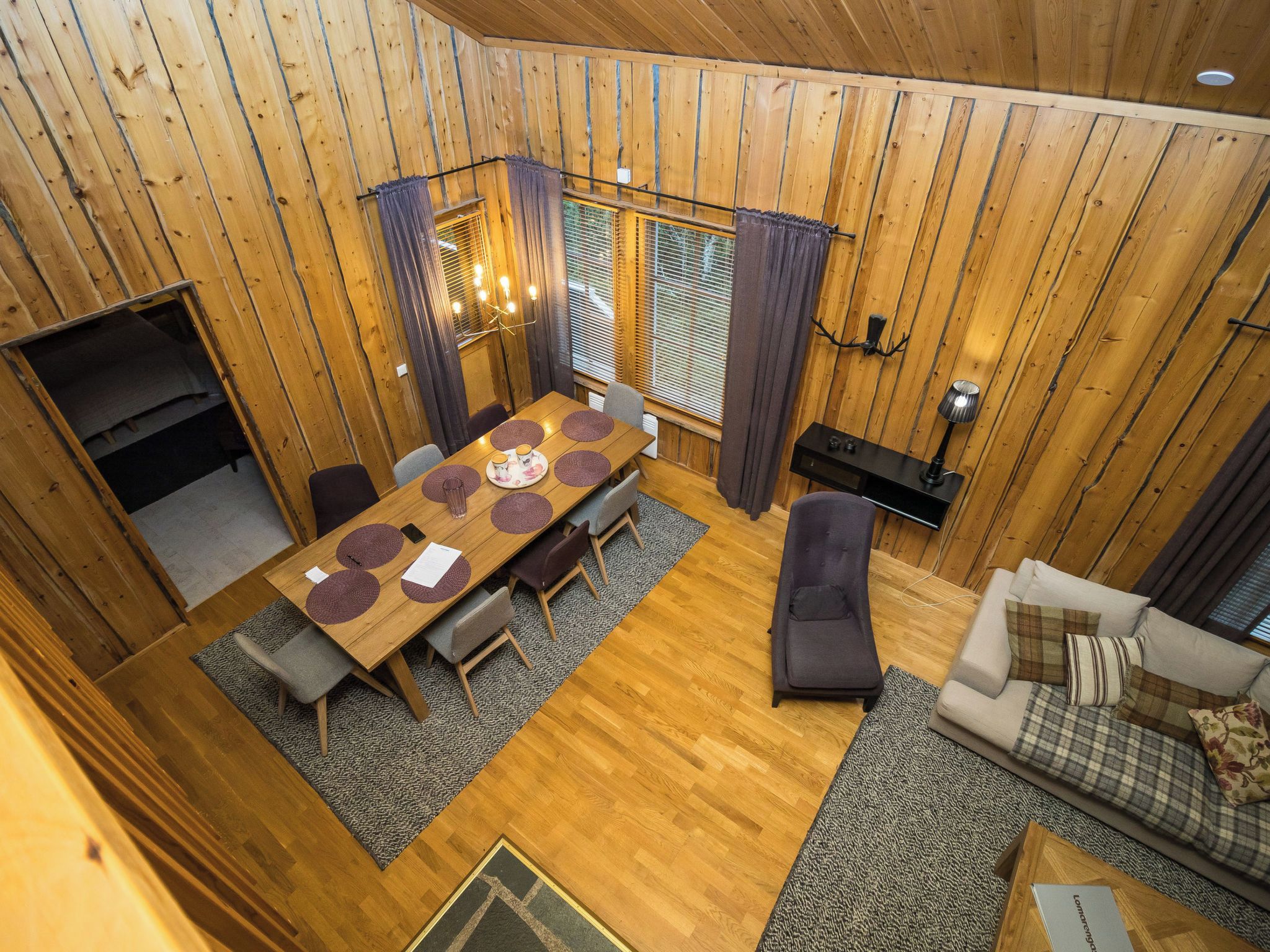 A wooden interior with a dining table, chairs, a sofa, and a television.