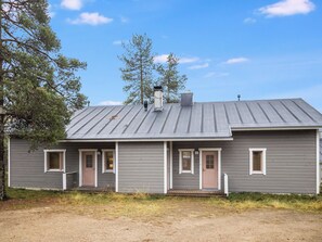 Een woonhuis met twee verdiepingen, een metalen dak, een voortuin en een veranda.