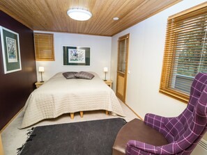 A bedroom with a bed, two bedside lamps, a framed picture on the wall, and a window with blinds.