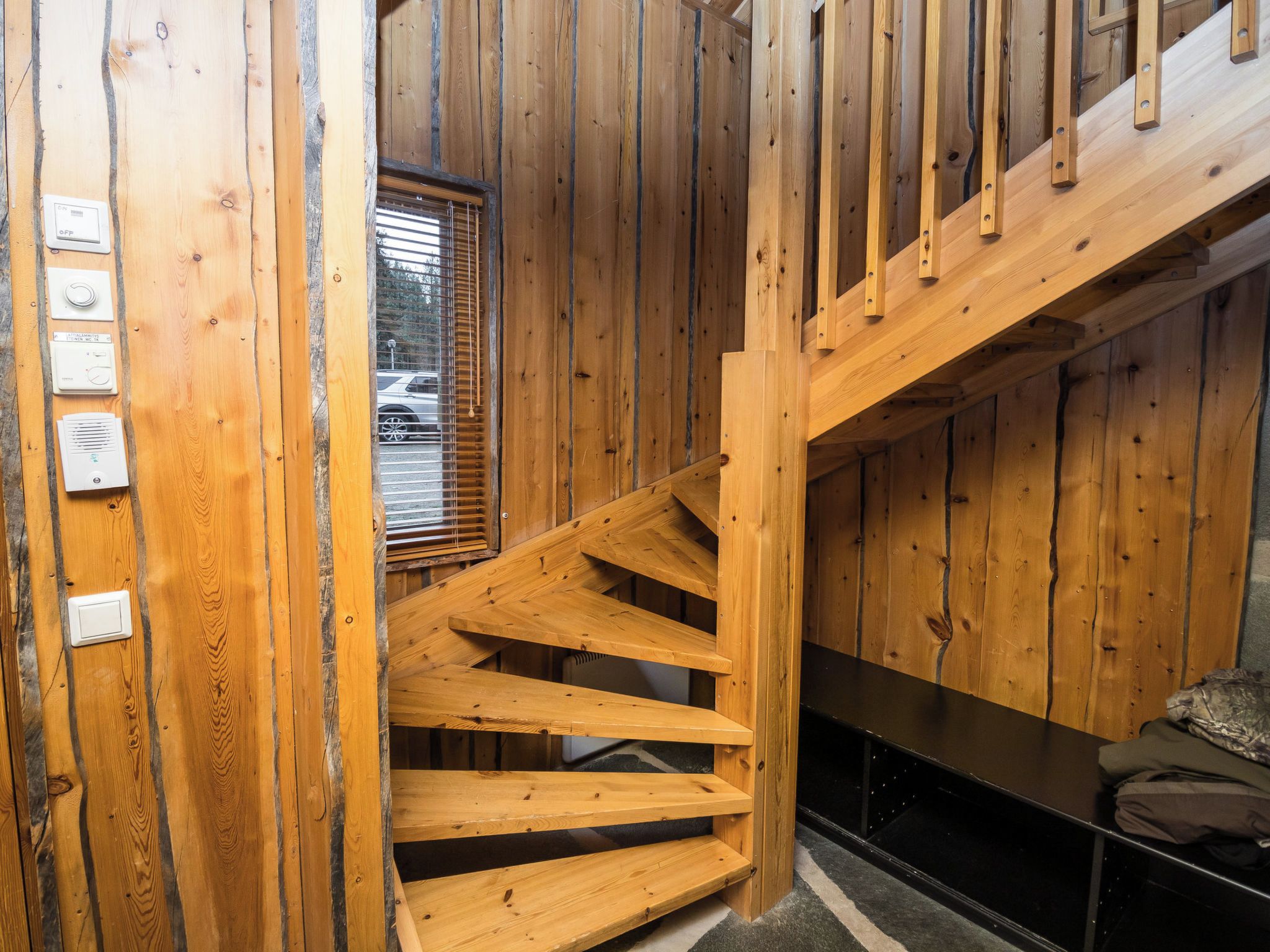 A wooden staircase leading to a second floor, with a window overlooking a parking area.