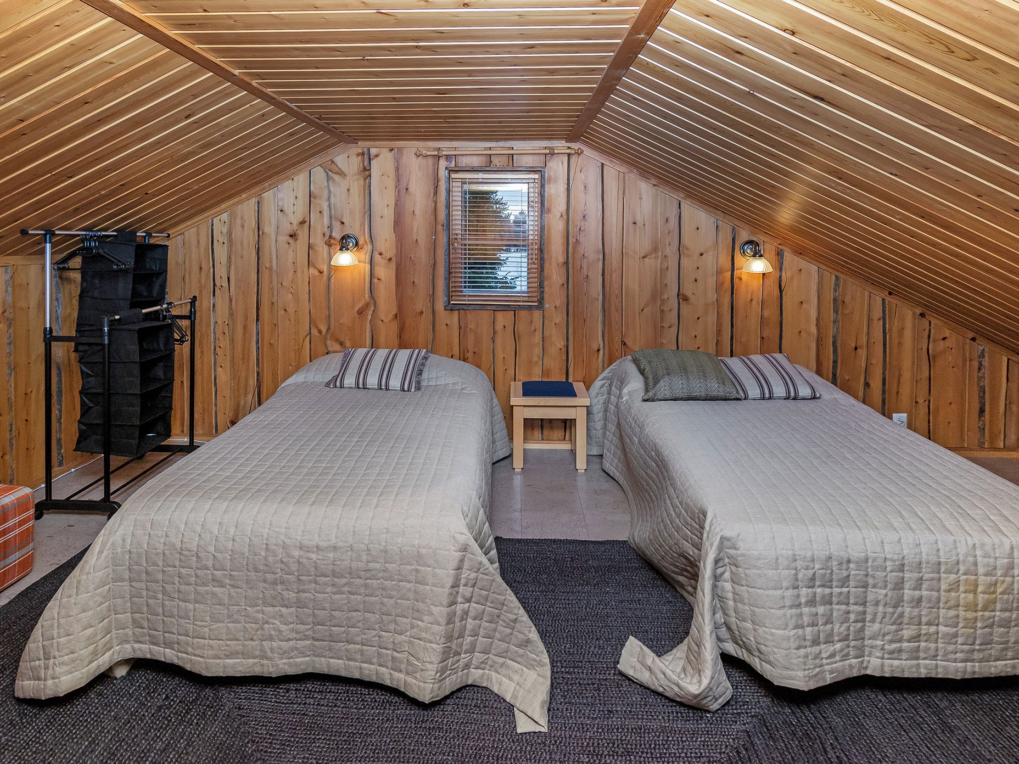 Une petite chambre mansardée avec deux lits, des murs en bois, une fenêtre et un ventilateur de plafond.