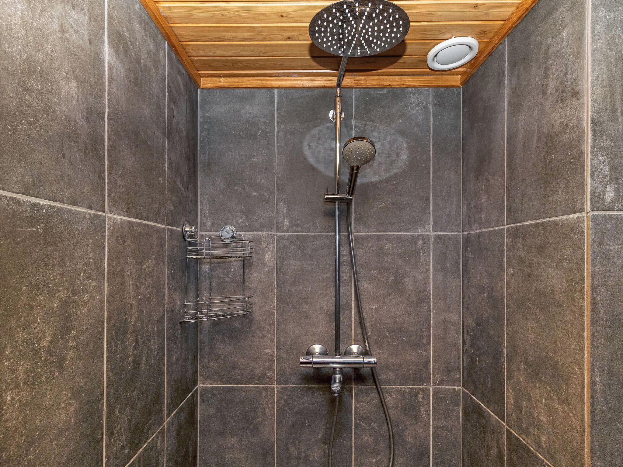 Una ducha con techo de madera, un cabezal de ducha manual y un grifo empotrado en la pared.