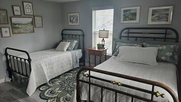 Une chambre avec deux lits, une petite table et une fenêtre avec des stores.
