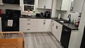 Een moderne keuken met witte kasten, een zwarte kookplaat en een raam met een plant.