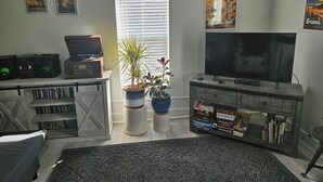 Een woonkamer met een televisie, een boekenkast, een bijzettafeltje en een potplant.