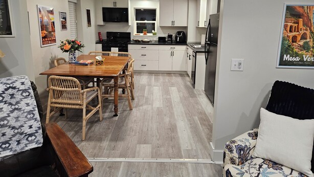 Een moderne keuken met witte kastjes, een eettafel met stoelen en een koelkast.