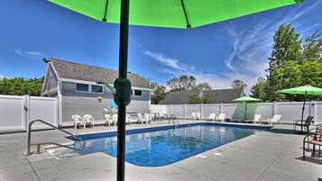 A backyard with a swimming pool, white chairs, and a green umbrella.