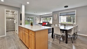 A modern kitchen with a central island, a dining area with a glass table, and a shower area with a glass door.