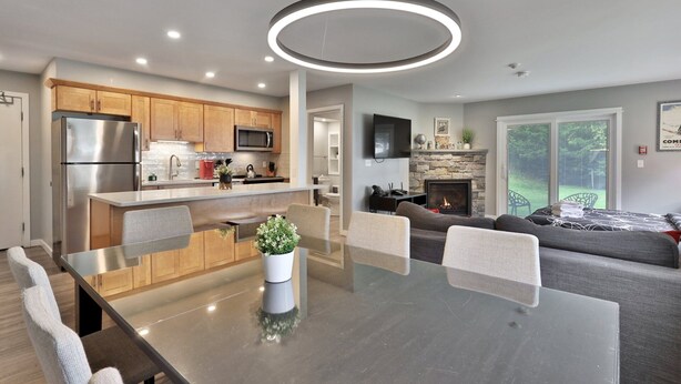 A modern kitchen with stainless steel appliances, a dining area with a glass table, and a living room with a fireplace.
