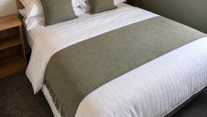 A bed with a wooden headboard, white bedding, and a green throw blanket. There are two bedside tables with lamps. - Caravan Georgi 3 Bed Balcony (Rhyl)