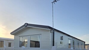 A mobile home with a white exterior, a fenced deck, and a satellite dish. - Caravan Georgi 3 Bed Balcony (Rhyl)