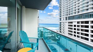 Ein Balkon mit Glasgeländer, der auf den Ozean, einen Pool und ein Gebäude mit rasterartiger Fassade blickt.