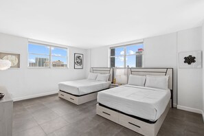 A modern bedroom with two beds, a desk, and a window with a city view. - Newly Renovated~Walk to Beach~Close to Entertainment + Nightlife and Shopping (Hollywood)