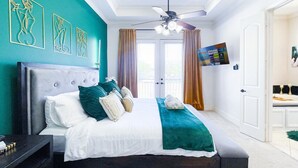 Une chambre moderne avec un grand lit, un ventilateur de plafond et des œuvres d’art accrochées aux murs.