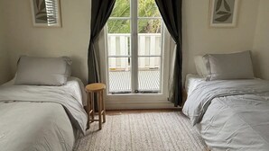 Une chambre avec deux lits, un petit tabouret et une fenêtre avec des rideaux.
