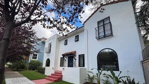 Une maison blanche à deux étages, avec une porte d’entrée rouge, un petit porche et une pelouse bien entretenue.