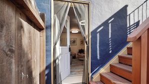 A wooden staircase leading to a room with a patterned floor, a door with curtains, and a view of a hallway with a ceiling light. - Coast PalmTree Yard 2BR Block from Beach (Pacifica)