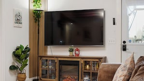 A living room with a flat-screen TV mounted on the wall, a wooden cabinet with glass doors, a fireplace, and a couch. - Coast PalmTree Yard 2BR Block from Beach (Pacifica)