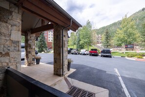 A stone building with a covered entrance, a parking lot with several cars, and a mountainous backdrop.