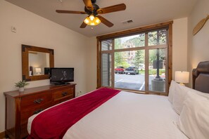 A hotel room with a bed, a television, a ceiling fan, a window with a view of the street, and a wooden dresser. - Experience comfort and adventure at Peregrine Point 103, a spacious 2-bedroom condo (Durango)